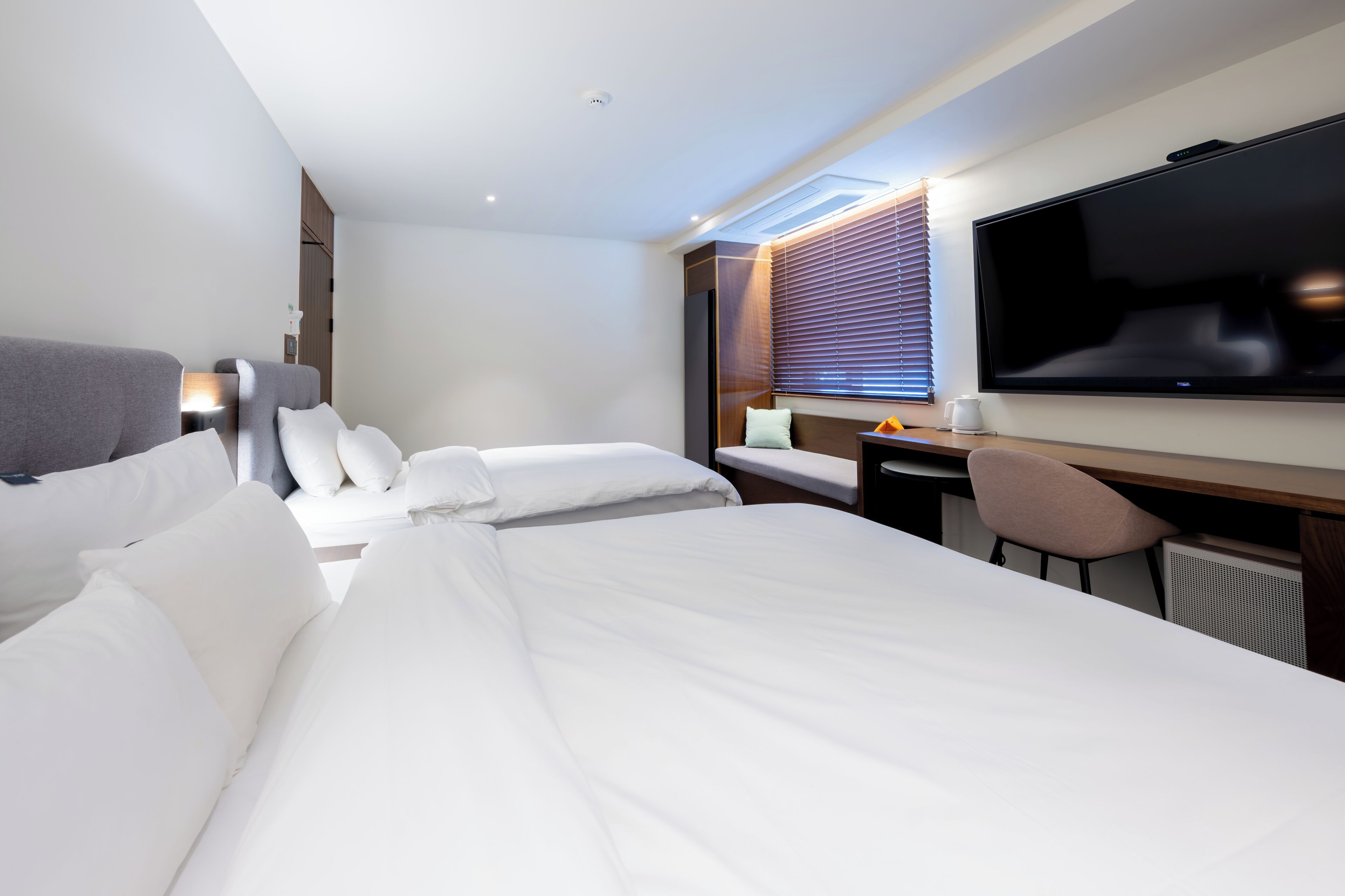 Habitación de hotel con cama, escritorio, silla, televisor y ventana con persianas.