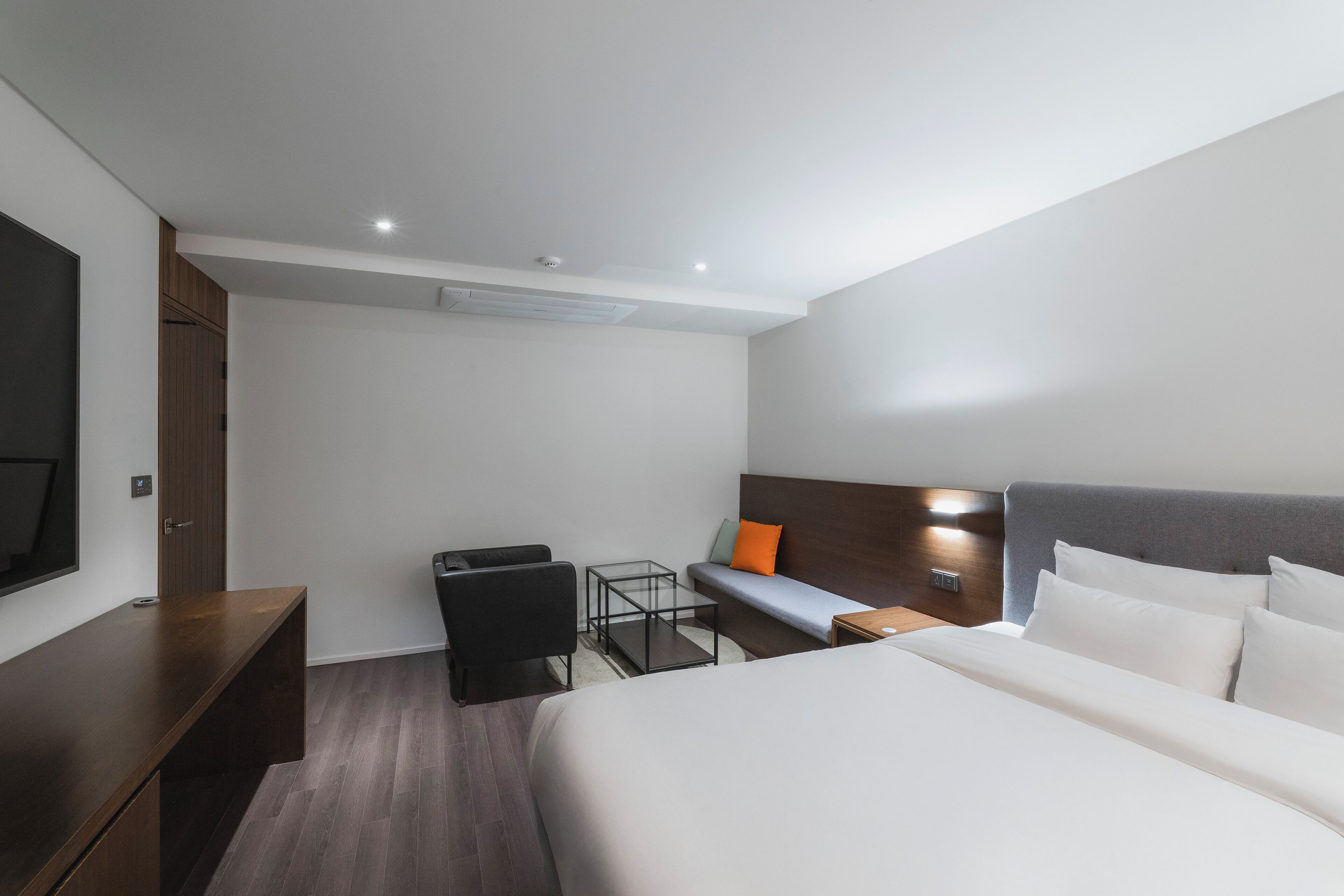 A modern hotel room with a large bed, a desk, a chair, and a TV.