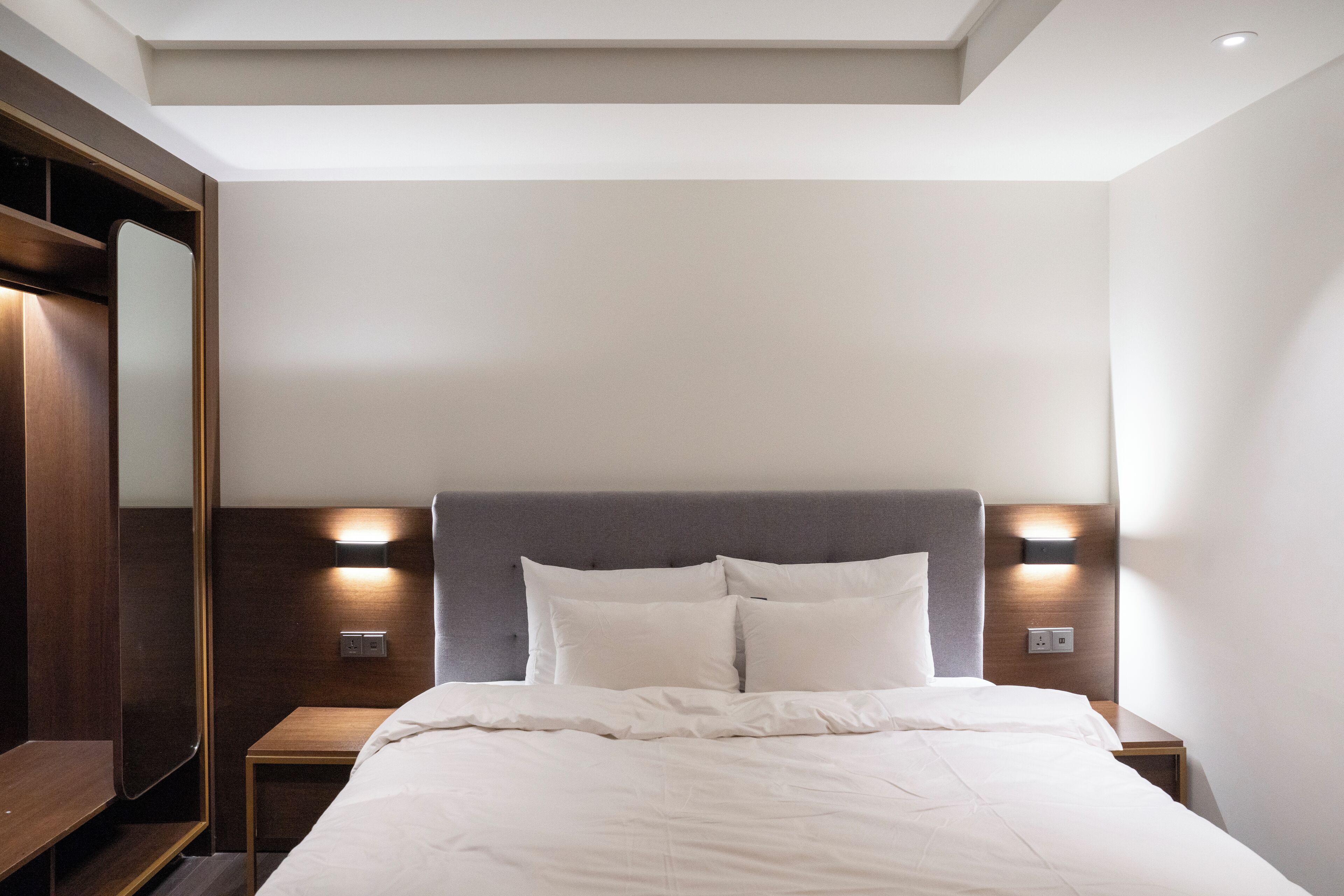 A neatly made bed with white linens, a wooden headboard, and two bedside lamps.