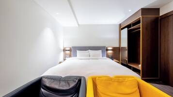 Une chambre d’hôtel moderne avec un grand lit, une armoire et un coin salon comprenant un fauteuil jaune et noir.
