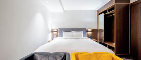 A modern hotel room with a large bed, a wardrobe, and a seating area with a yellow and black chair.