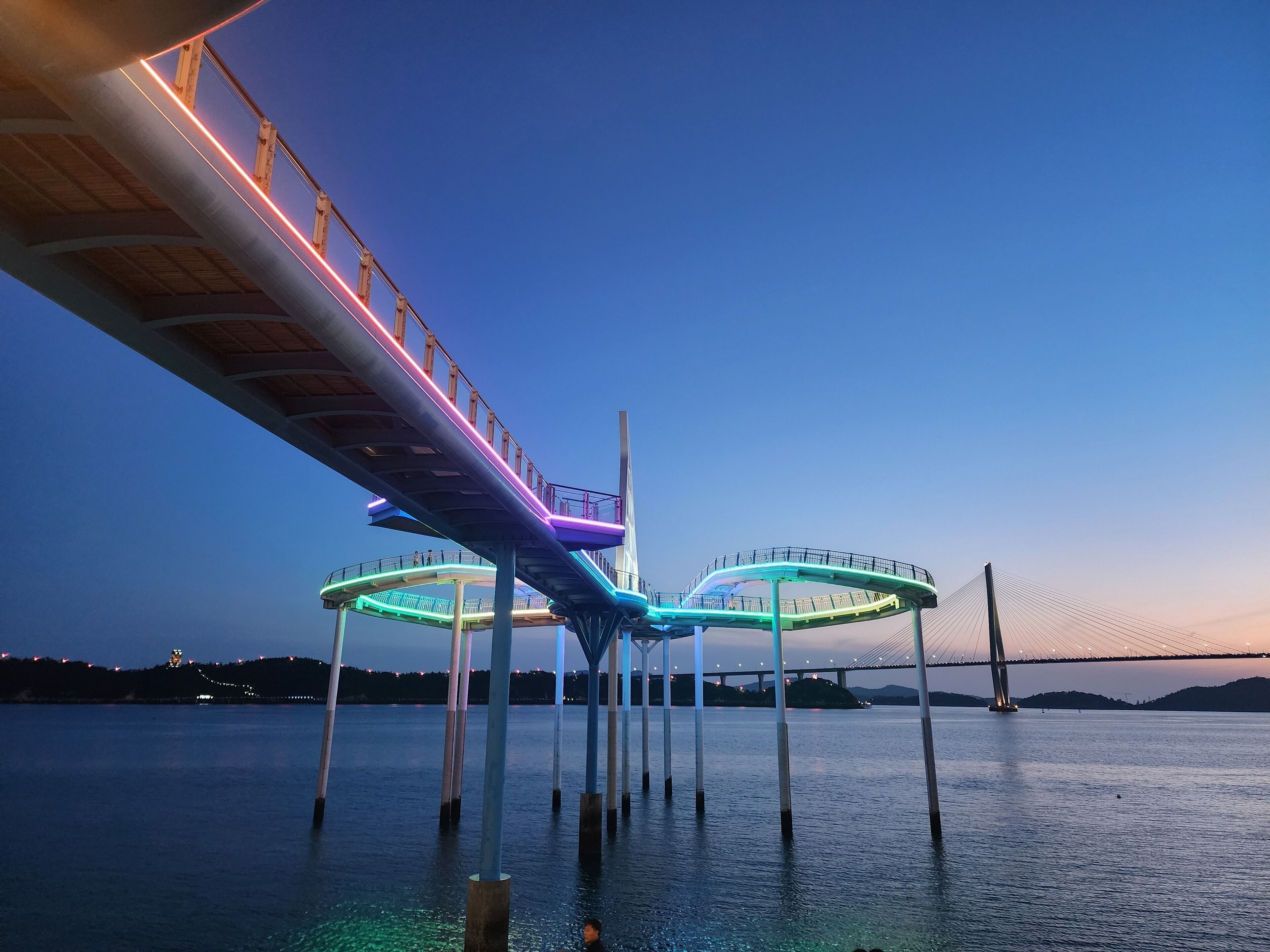 Een brug met verlichte voetpaden over water, ondersteund door pilaren.