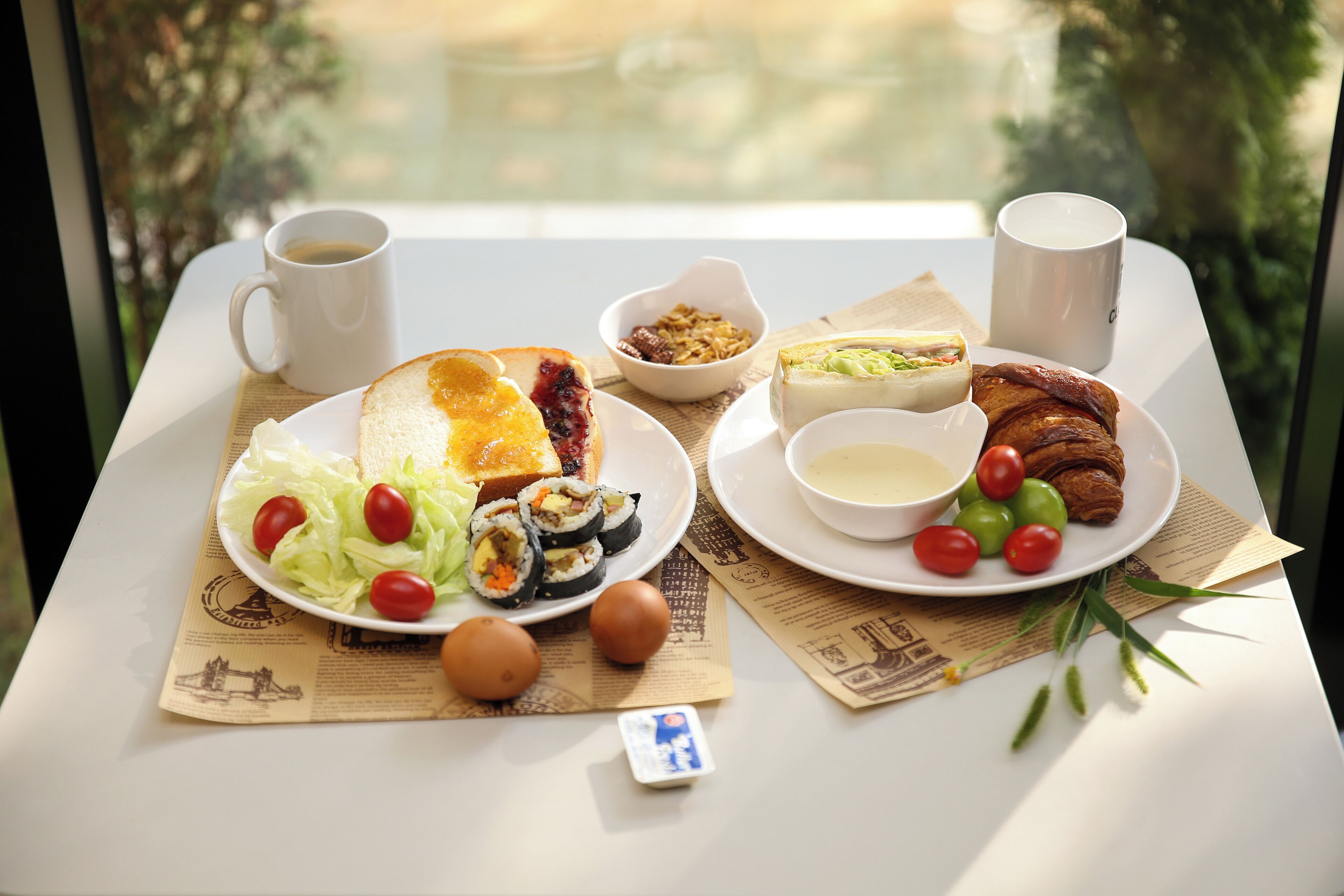 A table with a variety of food items including sushi, bread, and a croissant, along with two cups of coffee.