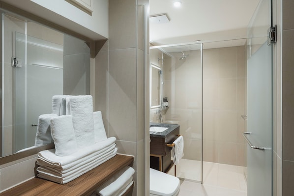 A modern bathroom with a glass shower enclosure, a wooden vanity with stacked towels, and a large mirror. - Yaja Hotel Peace Square branch (Mokpo)