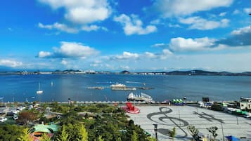 A waterfront park with a large open space, a red sculpture, and a view of the sea and distant cityscape.