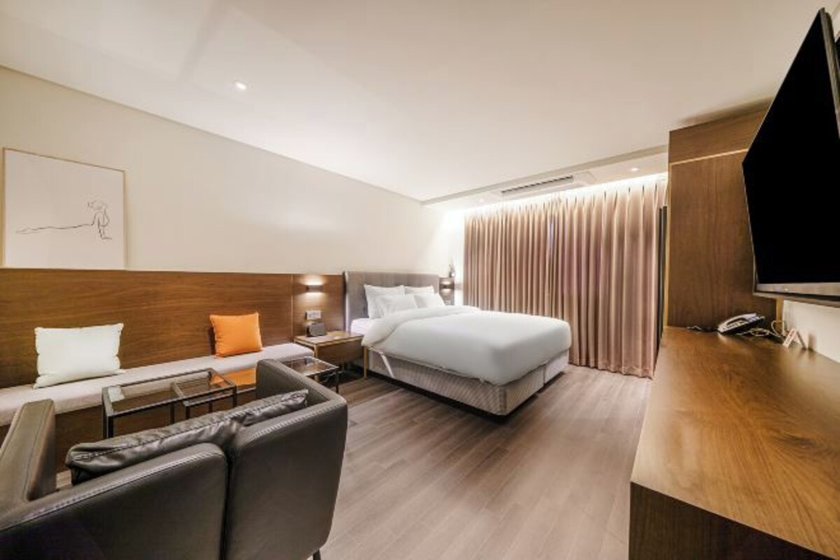A modern hotel room with a bed, a desk, a sofa, and a TV.