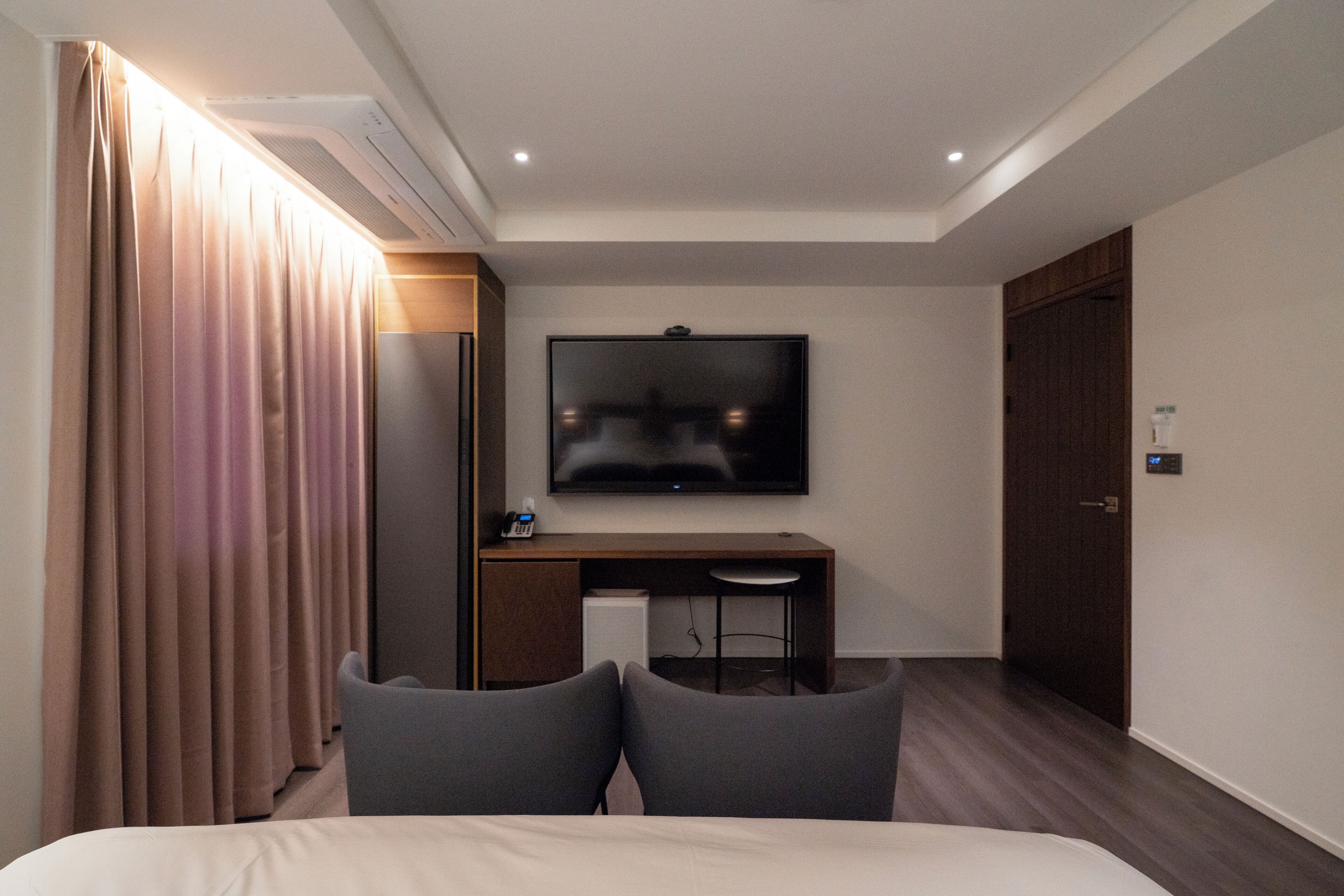 A hotel room with a bed, a desk with a chair, a television, and a wardrobe.
