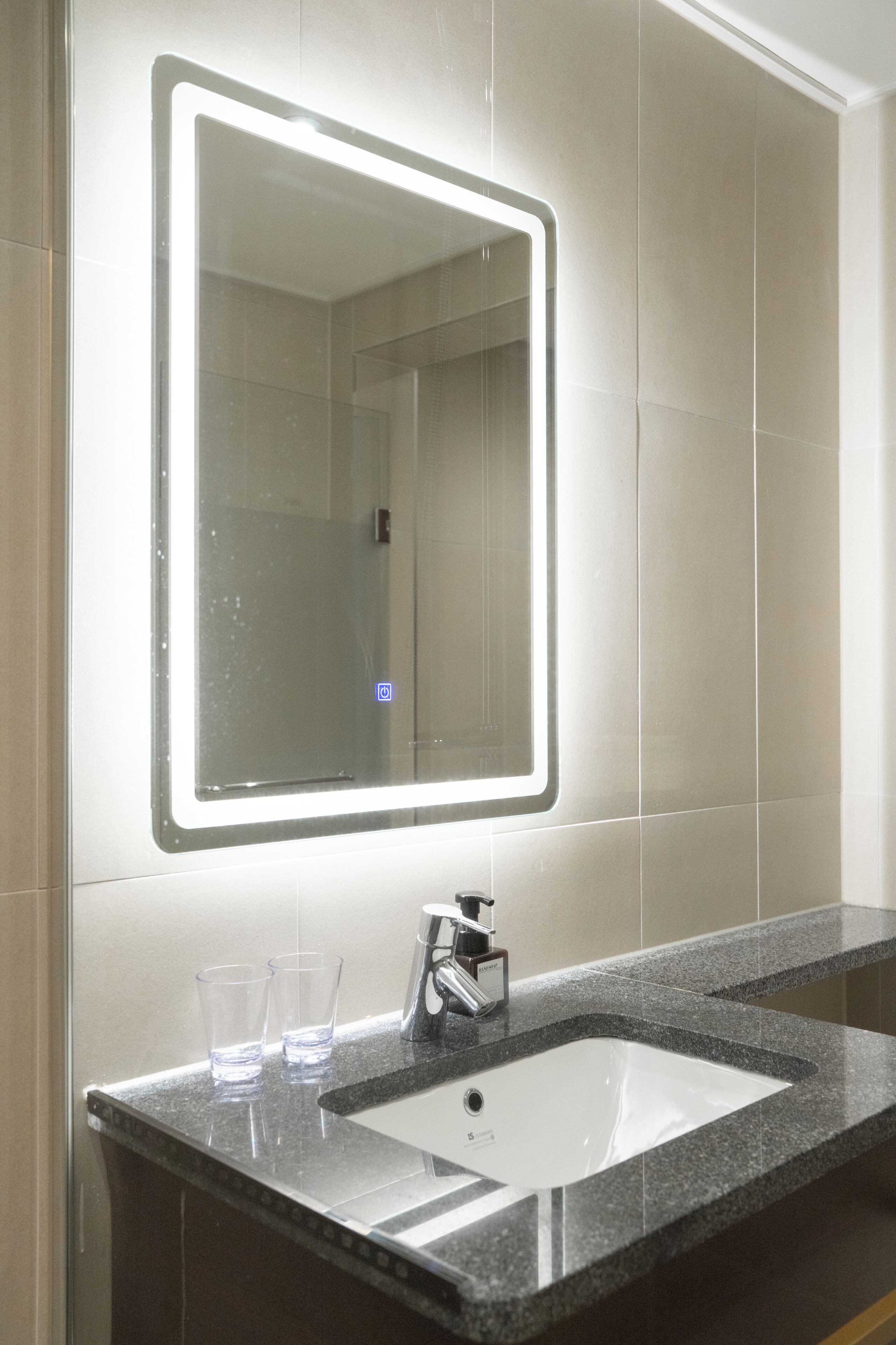 Un baño con un espejo grande, un lavabo y dos vasos sobre el mostrador.