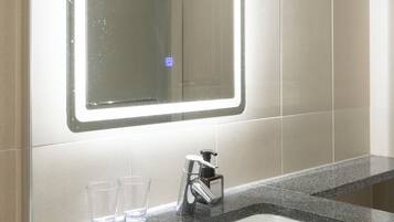 Un baño con un espejo grande, un lavabo y dos vasos sobre el mostrador.