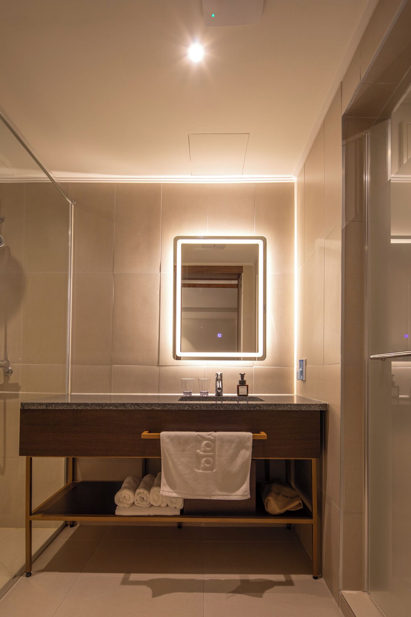 Un baño moderno con un espejo grande, un tocador con toallero y una zona de ducha.
