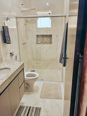 A modern bathroom with a glass-enclosed shower, a toilet, and a vanity with a marble countertop.