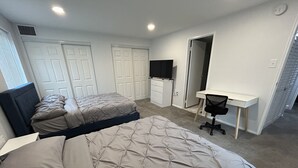 Ein Schlafzimmer mit zwei Betten, einem Schreibtisch, einem Stuhl und einem Fernseher.