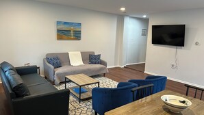 Ein Wohnzimmer mit einer Couch, Sesseln, einem Couchtisch und einem an der Wand befestigten Fernseher.