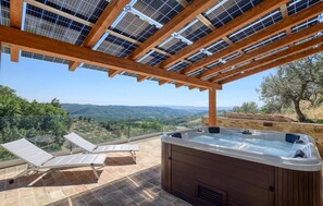 Ein Whirlpool unter einer Pergola mit Solarmodulen, mit Blick auf eine reizvolle Landschaft.