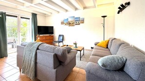 A living room with a grey sofa, a wooden cabinet, a TV, and a wall with framed pictures. - 3 bedroom beautiful home in Bredene (Bredene)