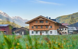 A multi-story wooden building with balconies, set in a mountainous area with a field in the foreground. - moderne Ferienwohnung (Längenfeld)