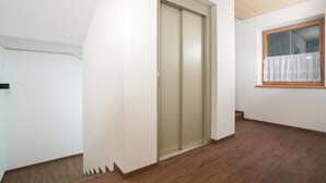 Un corridoio con pavimento in legno, una porta scorrevole e una finestra con tenda bianca.