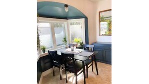 Un coin repas avec une table et des chaises, une fenêtre avec des stores et un tableau accroché au mur.