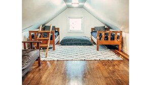 Une petite chambre mansardée avec deux lits superposés, une fenêtre et un plancher en bois.