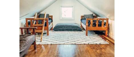 A small attic bedroom with two bunk beds, a window, and a wooden floor.