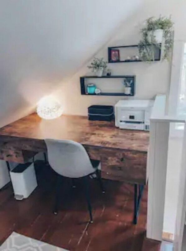 A home office with a wooden desk, a chair, a printer, and shelves with decorative items.