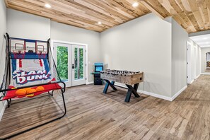 A room with a basketball hoop, a foosball table, and a door leading to a green outdoor area.