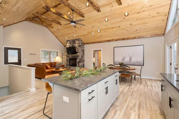 A spacious living area with a fireplace, a dining table, and a kitchen island. - Sam's Place: Brand-new Massanutten custom home- Flat driveway & Mountain Views! (Massanutten)