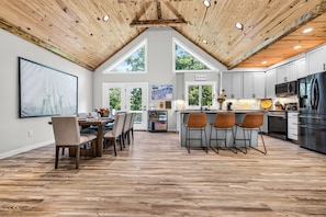 A spacious kitchen with a central island, wooden ceiling, and large windows.