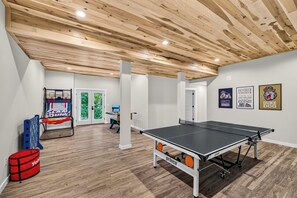 A room with a ping pong table, a basketball hoop, and a table tennis table.