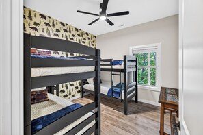A bunk bed room with a ceiling fan, a window with a view of trees, and a small table.