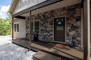 A house with a stone facade, a wooden porch, and a welcome mat. - Sam's Place - Custom 6BR Home - Arcade, Games, Movie Room & Hot Tub! (Massanutten)