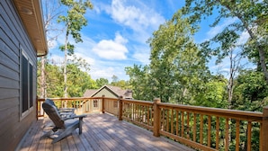 A wooden deck with a railing, a bench, and a view of a house and trees.