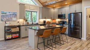 A modern kitchen with a large island, bar stools, stainless steel appliances, and a wooden ceiling.