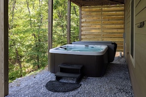 Un jacuzzi en un área exterior techada con terraza de madera y vistas a un bosque.