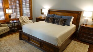 Un dormitorio ordenado con una cama grande, dos mesitas de noche, una silla y una pequeña mesa.