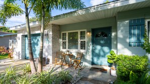 A two-story house with a front porch, a blue door, and a small garden area with chairs and plants.