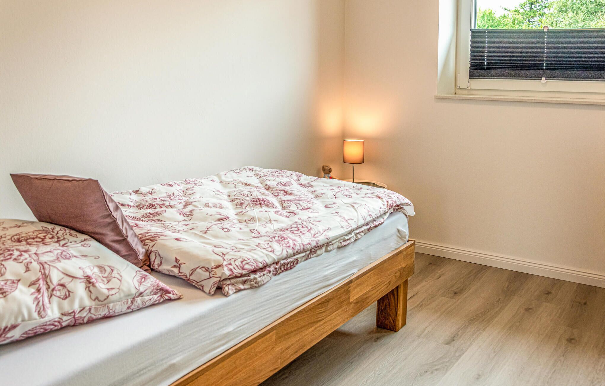 A single bed with a floral bedspread, a wooden headboard, and a nightstand with a lamp.