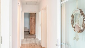 Un couloir doté d’un plancher en bois, de murs blancs et d’une porte donnant sur un escalier.