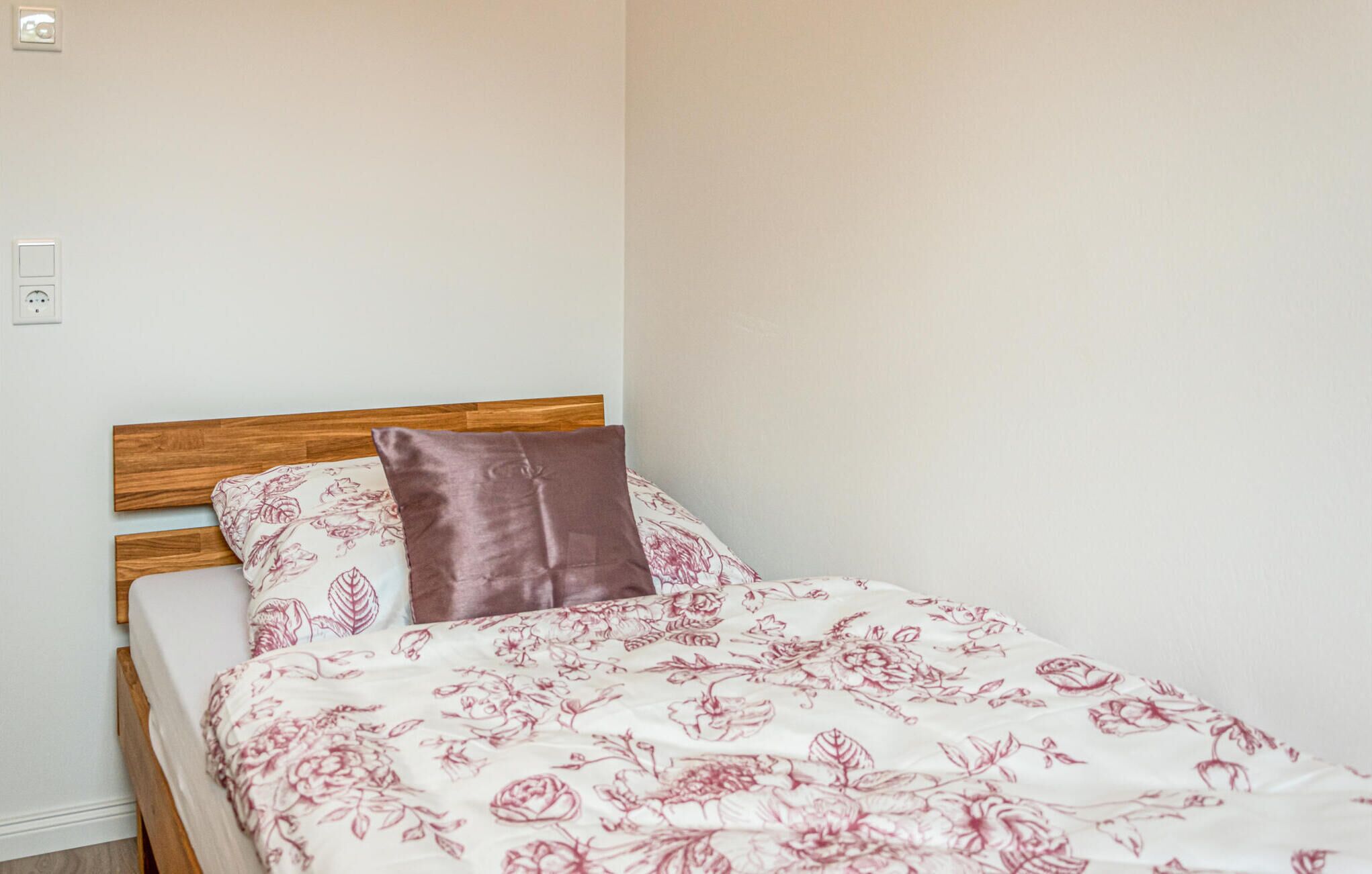 A single bed with a wooden headboard, a floral-patterned bedspread, and a brown pillow.