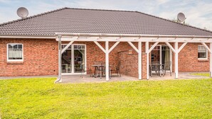 Une maison en briques avec un toit en tuiles, des antennes paraboliques et un patio couvert équipé de chaises et de tables.
