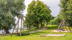 Un parc avec des balançoires, un banc et un sentier longeant un plan d’eau.