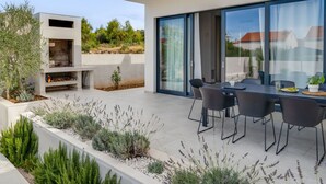 A modern outdoor patio with a dining area, a built-in grill, and a variety of plants. - Wonderful private villa for 8 guests with WIFI, private pool, A/C, TV and terrace (Vodice)