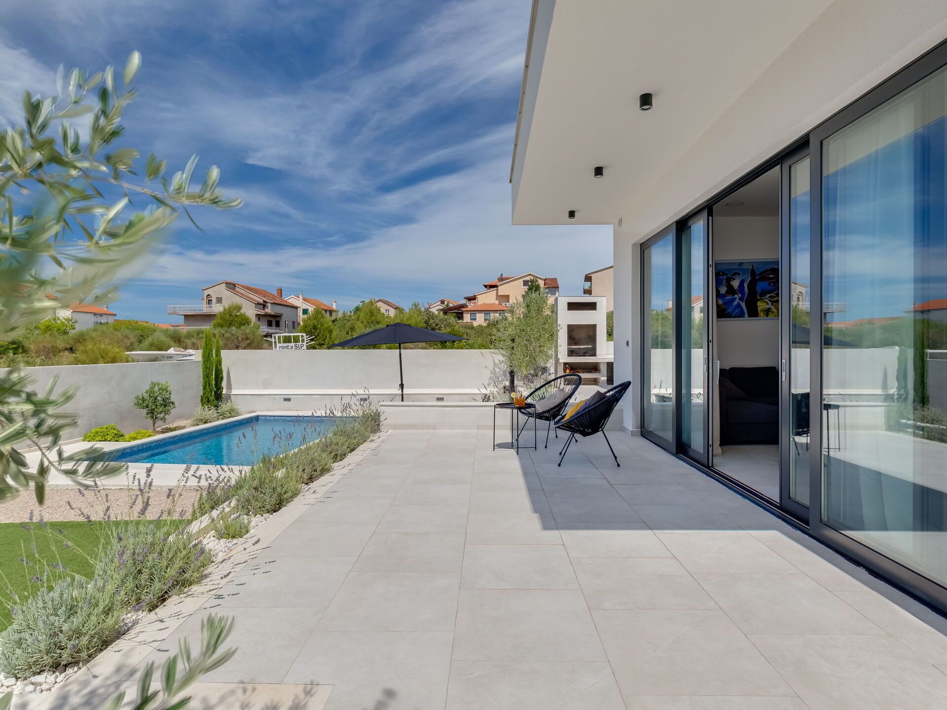 A modern outdoor patio with a swimming pool, a glass-enclosed dining area, and a view of neighboring houses.