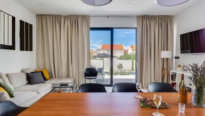 A modern hotel room with a large wooden dining table, a sofa with cushions, a TV, and a balcony with a view of buildings. - Wonderful private villa for 8 guests with WIFI, private pool, A/C, TV and terrace (Vodice)
