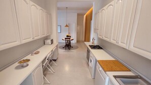 Una cucina moderna con mobili bianchi, un'isola centrale dotata di piano cottura e una zona pranzo con tavolo e sedie.