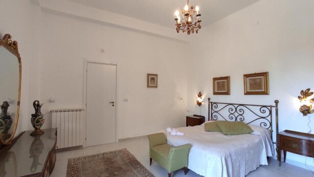 Een slaapkamer met een bed, een stoel, een dressoir, een spiegel en een kroonluchter.
