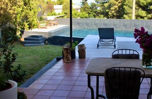 A patio with a pool, outdoor furniture, and a view of the surrounding greenery.