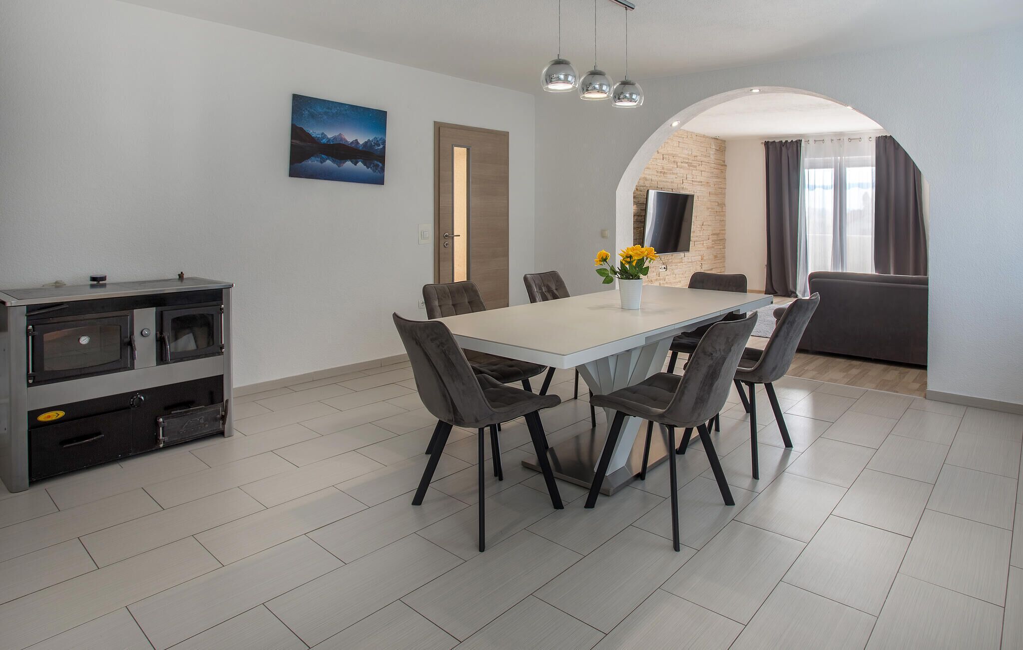 Un espace repas moderne avec une table blanche, des chaises grises et un four encastré.