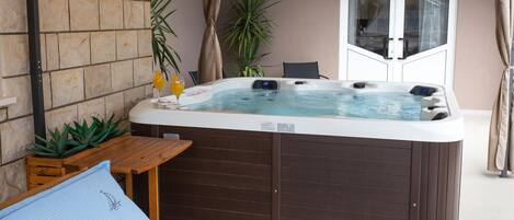 Ein Whirlpool mit Holztisch und Stühlen, umgeben von Topfpflanzen und einem Fenster mit Vorhängen.