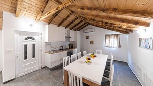 Una cuina compacta amb armaris blancs, una taula de dinar amb cadires i un sostre de fusta.